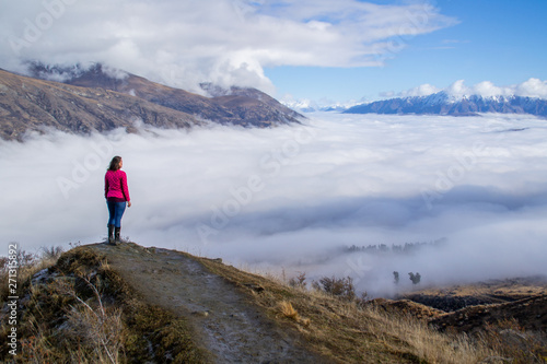 Low clouds or fog (inversion) above lake Wakatipu and Queenstown valley. View of the scenic road and snow covered peaks of Single cone, Cecil Peak and Mount Nicholas. Panoramic landscape. New Zealand.