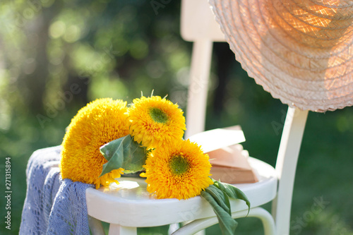 Yellow sunflowers, book and straw hat are on wooden white chair. Summer still life in garden. photo