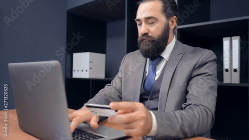 Beardy Businessman Making Online Payment. Holding Card In Hand While Typing On Laptop. Business Concept. photo