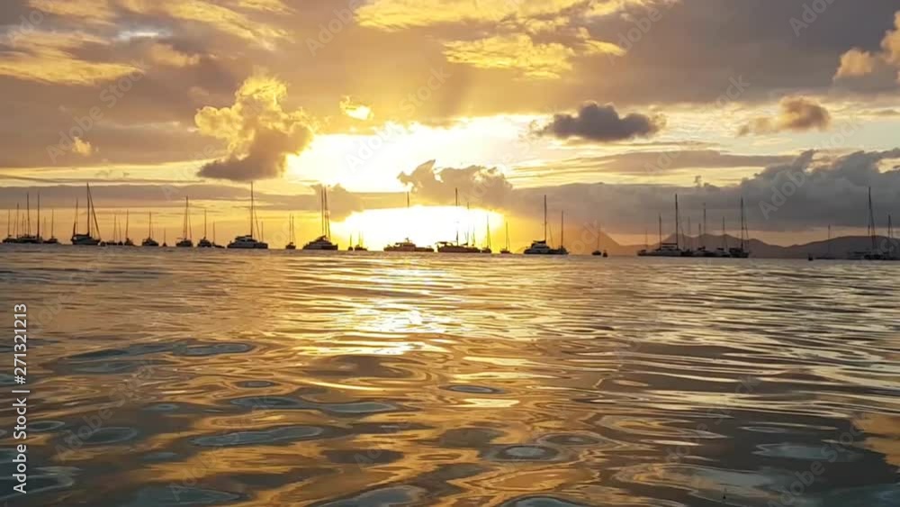 Golden water at sunset with sailboats floating in the background Golden water at sunset with sailboats floating in the background