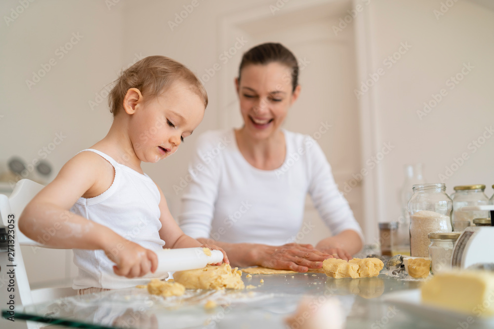 Mother and little daughter with dough roll making a cake together in kitchen at home Mother and little daughter with dough roll making a cake together in kitchen at home