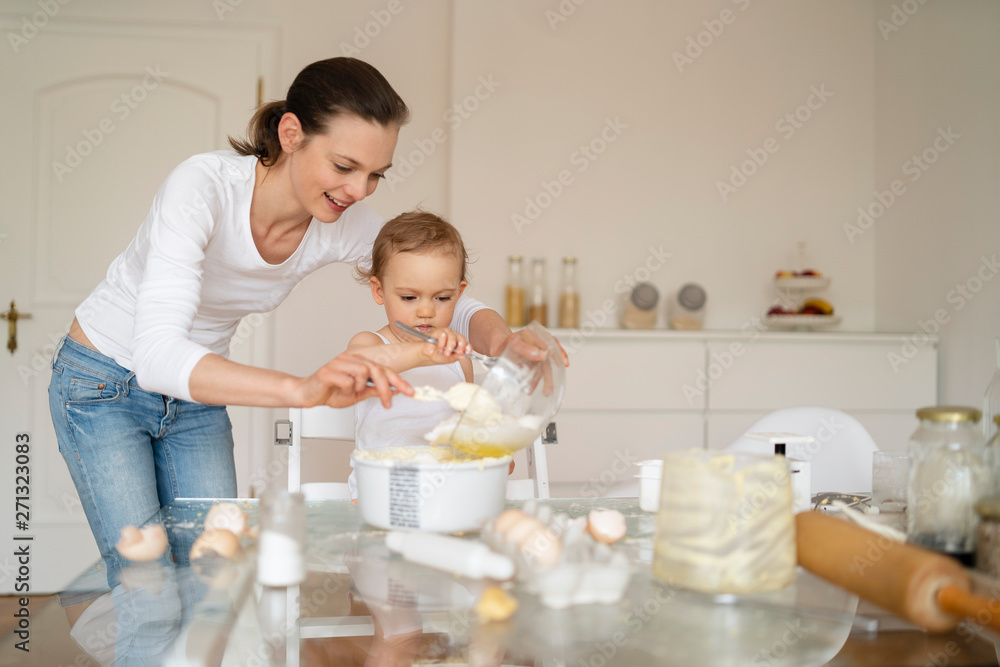 Mother and little daughter making a cake together in kitchen at home Mother and little daughter making a cake together in kitchen at home