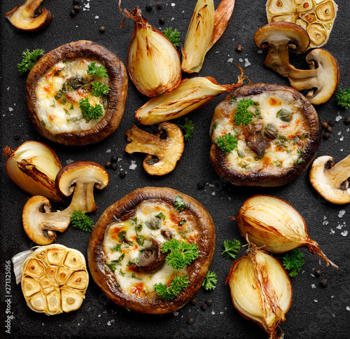 Stuffed portobello mushrooms stuffed with mozzarella and gorgonzola cheese and aromatic herbs on a black background, top view. Vegetarian food photo