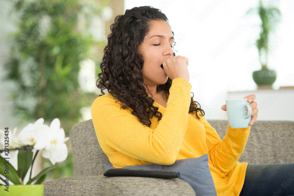 Fototapeta premium sleepy woman holding hot drink on knee on sofa