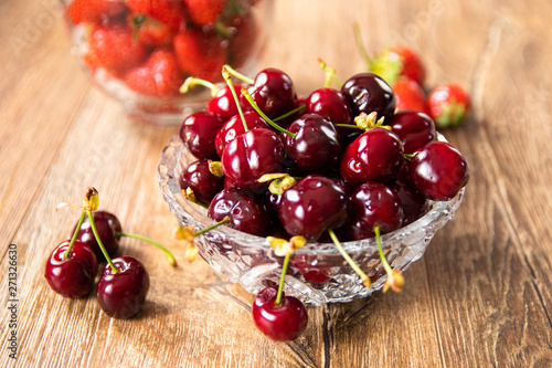 Fresh organic sweet cherries and strawberries in a glass bowls on wooden table