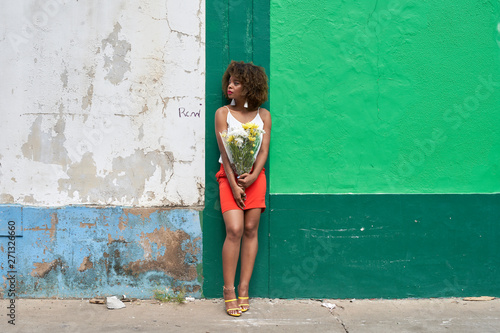 Young woman with bunch of flowers leaning against wall looking around photo