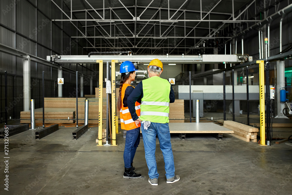 Rear view of male and female worker standing in factory workshop Rear view of male and female worker standing in factory workshop