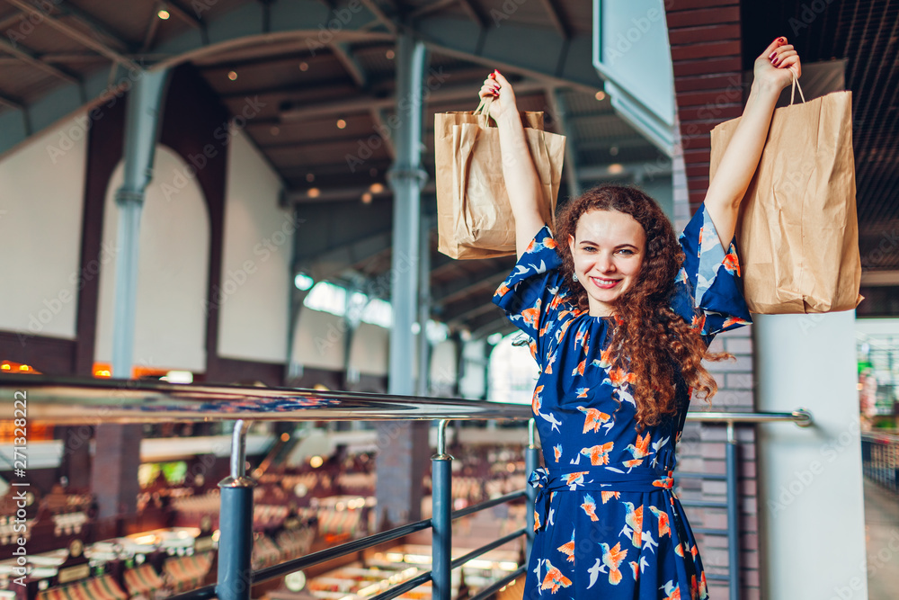 Young happy woman raising hands with shopping paper bags in shopping center.