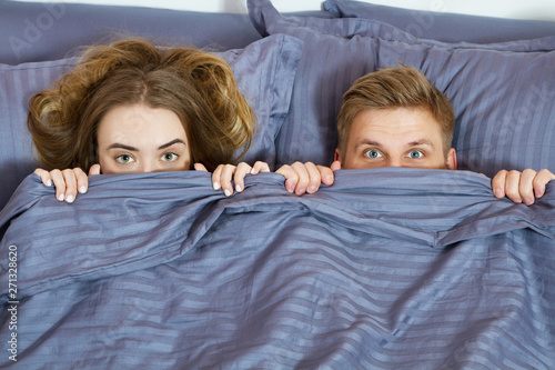 adult couple hiding under blanket in bed . Couple in bedroom in the morning.