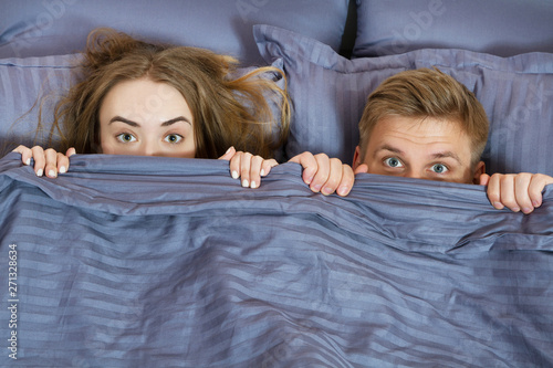 happy couple hiding under blanket in bed . Couple in bedroom in the morning.