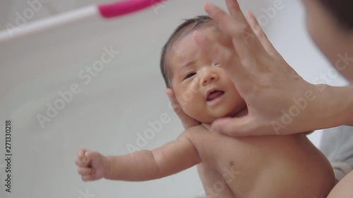 Portrait of asian newborn baby girl is washing face and taking bath by her father in white plastic tub in bathroom at home.