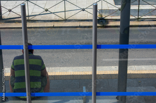 Sad man sitting at blue stripped bus stop on sunny day