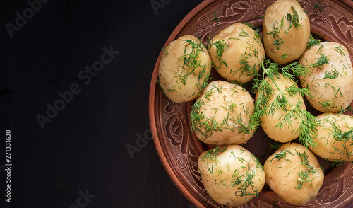 Boiled potatoes with dill in a plate on a black wooden table.