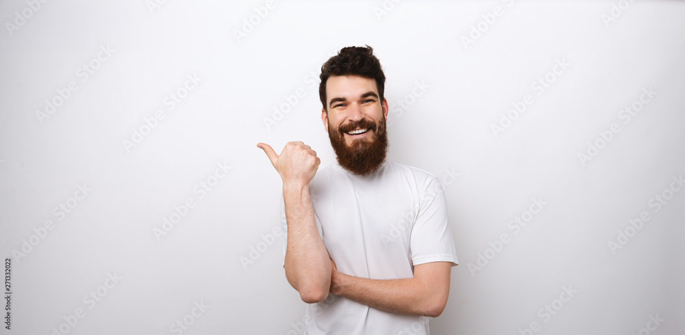 Portrait of cheerful bearded man in white t-shirt pointing away at copyspace Portrait of cheerful bearded man in white t-shirt pointing away at copyspace