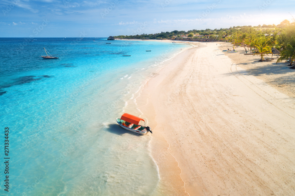 Aerial view of the fishing boat in clear blue water at sunset in summer. Top view of boat, sandy beach, palm trees. Indian ocean. Travel in Zanzibar, Africa. Colorful landscape with motorboat, sea Aerial view of the fishing boat in clear blue water at sunset in summer. Top view of boat, sandy beach, palm trees. Indian ocean. Travel in Zanzibar, Africa. Colorful landscape with motorboat, sea