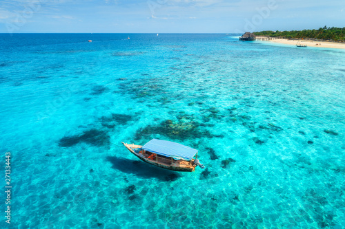 Aerial view of the fishing boat in clear blue water at sunny day in summer. Top view from the air of boat, sandy beach. Indian ocean in Zanzibar, Africa. Colorful Landscape with motorboat, clear sea © den-belitsky