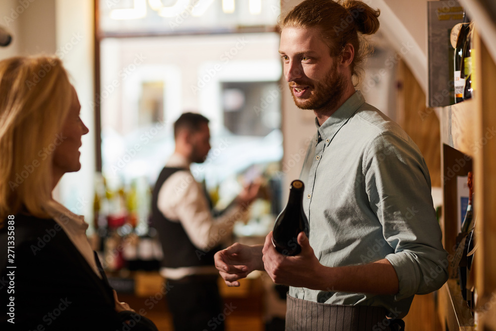 Waist up portrait of smiling young man consulting customer in liquor store, copy space