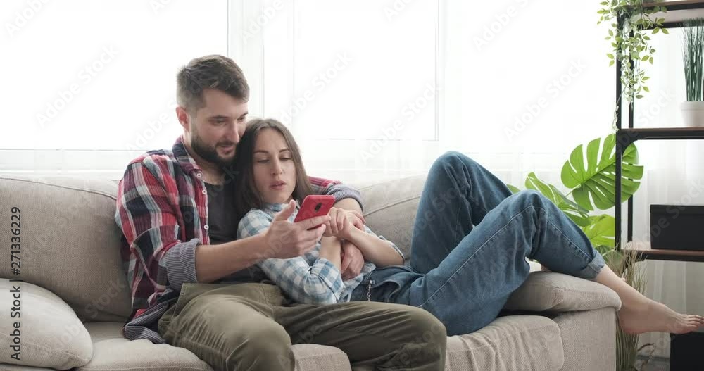 Relaxed couple lying on sofa and using mobile phone at home Relaxed couple lying on sofa and using mobile phone at home