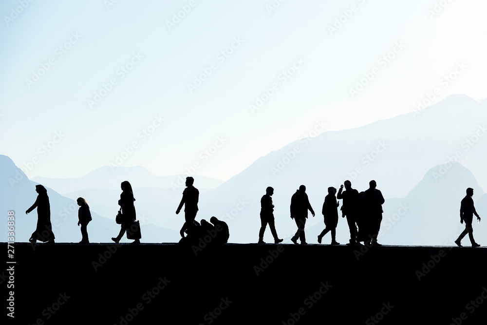 Silhouetted people walking and relaxing on street over sunny morning sky with high mountains in Antalya, Turkey
