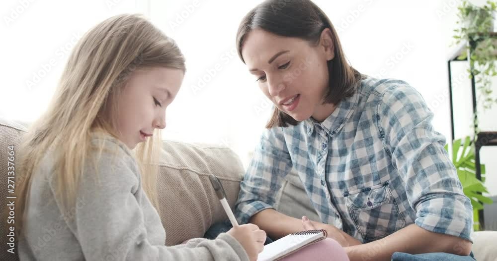 Smiling mother helping her daughter drawing on notepad at home Smiling mother helping her daughter drawing on notepad at home