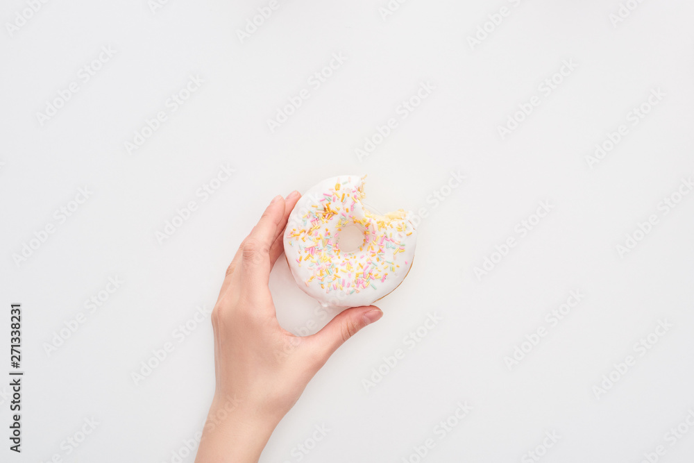 partial view of woman holding glazed bitten white doughnut with sprinkles on white background partial view of woman holding glazed bitten white doughnut with sprinkles on white background