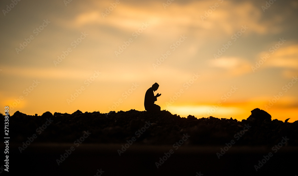 Concept of religion Islam. Silhouette of man praying on the background of a mosque at sunset