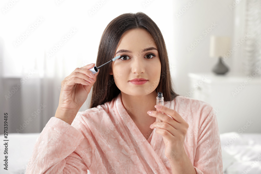 Beautiful woman applying oil onto her eyelashes indoors Beautiful woman applying oil onto her eyelashes indoors