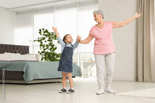 Cute girl and her grandmother dancing at home