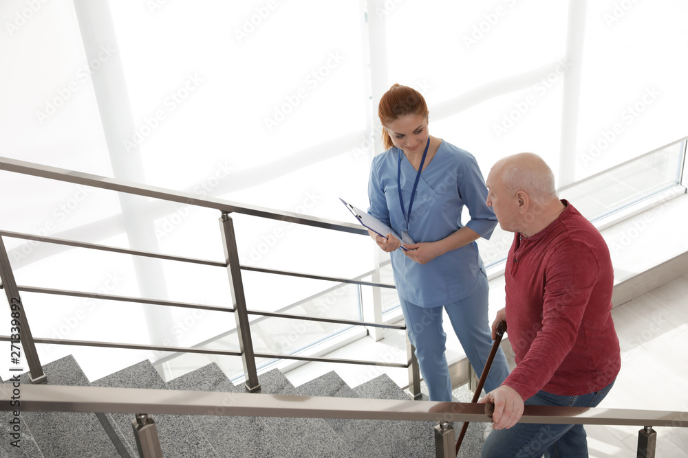 Nurse assisting senior man with cane to go up stairs indoors