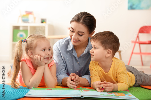 Kindergarten teacher reading book to children indoors. Learning and playing