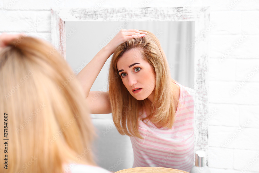 Young woman with hair loss problem near mirror indoors Young woman with hair loss problem near mirror indoors
