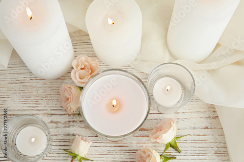 Flat lay composition with burning aromatic candles and roses on wooden table