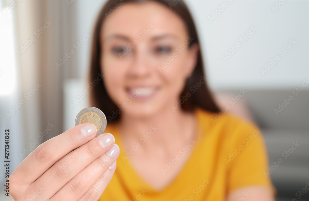 Young woman holding coin at home, focus on hand Young woman holding coin at home, focus on hand