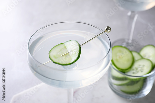 Glass of martini with cucumber on light table, closeup
