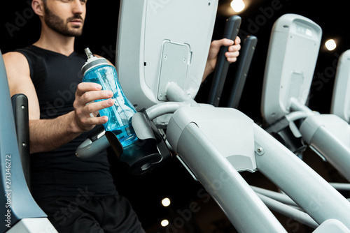 selective focus of handsome bearded man taking sport bottle working out on exercise bike