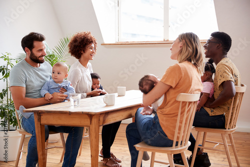 Two Families With Babies Meeting And Talking Around Table On Play Date At Home