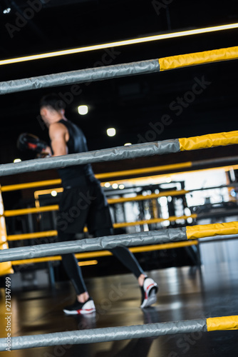 selective focus of boxing ring surrounded by ropes near man exercising in boxing gloves