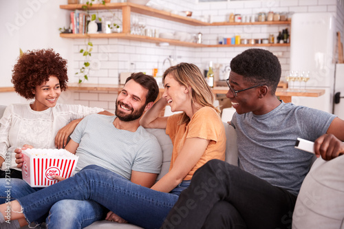 Group Of Friends Sitting On Sofa And Watching Movie At Home Whilst Eating Popcorn © Monkey Business