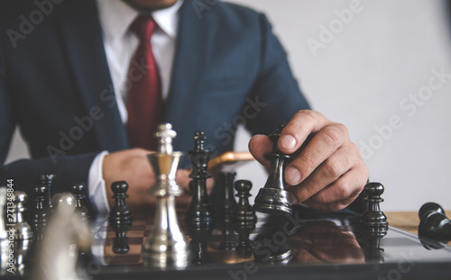 Retro style image of a businessman with clasped hands planning strategy with chess figures on an old wooden table.