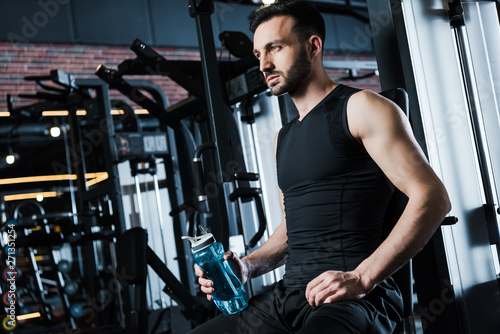 low angle view of handsome sportsman in sportswear holding sport bottle in gym