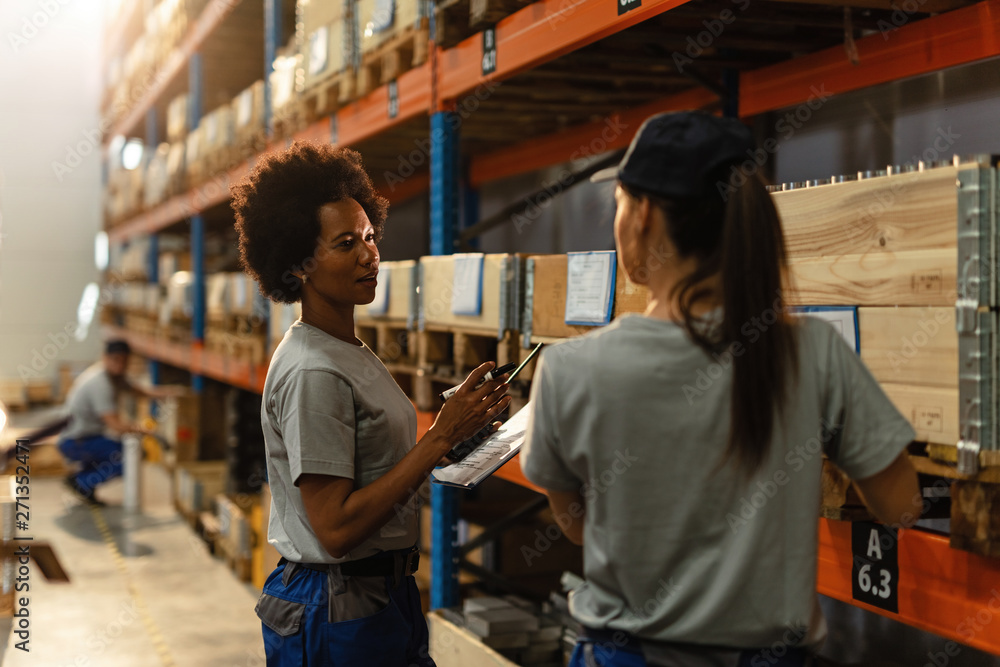 Female warehouse workers communicating in industrial storage compartment.