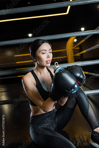 attractive woman with closed eyes holding sport bottle while wearing boxing gloves