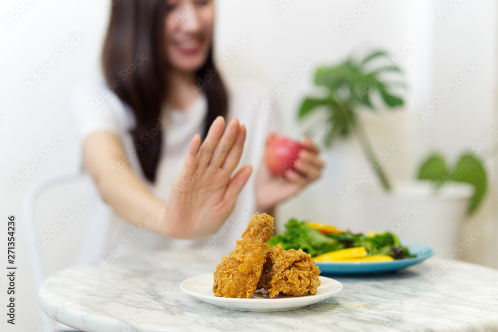 Young girl on dieting for good health concept. Close up female using hand reject junk food by pushing out her favorite fried chicken and choose red apple and salad for good health at home.