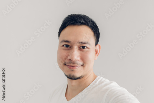 Smile man is taking selfie of himself with white t-shirt and grey background.