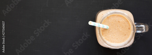 Banana apple smoothie in a glass jar over black surface, top view. Flat lay, from above, overhead. Copy space.