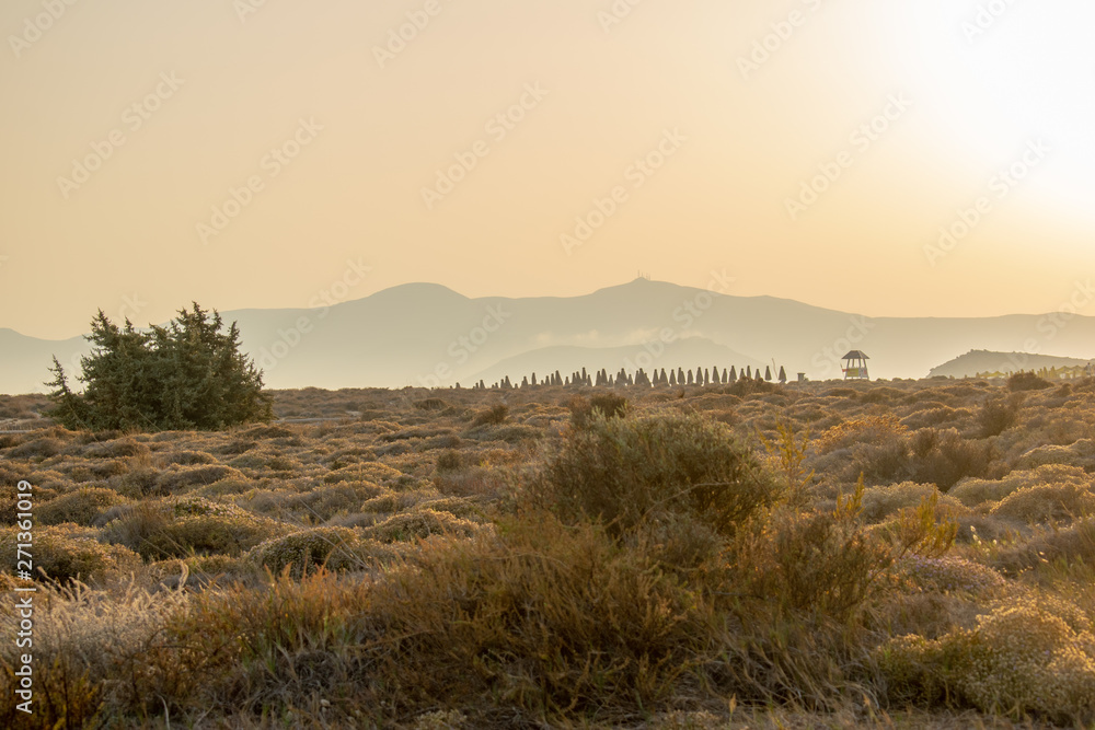 Sun sets over the mountains and bushy hills at a beach in the island of Naxos.