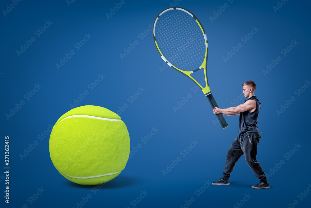 Small man in black sport clothes holding big tennis racket in hands with  yellow tennis ball on blue background 素材庫相片| Adobe Stock