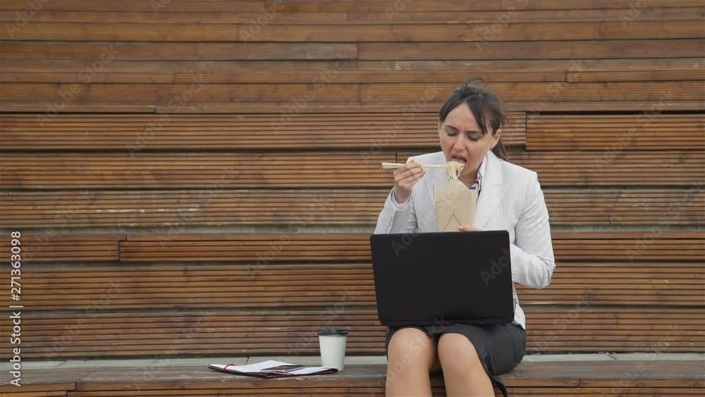 Businesswoman Eating Junk Food while Using a Laptop in Slow Motion. She is Working Outdoors during Lunch Break. Lifestyle and Business Concept Businesswoman Eating Junk Food while Using a Laptop in Slow Motion. She is Working Outdoors during Lunch Break. Lifestyle and Business Concept