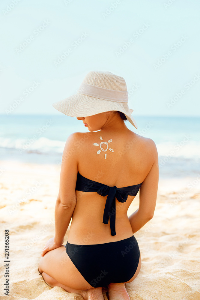 Woman Applying Sun Cream Creme on Tanned  Shoulder In Form Of The Sun. Sun Protection. Skin Care. Girl Using Sunscreen to Skin. Portrait Of Female Holding Suntan Lotion and Moisturizing Sunblock.