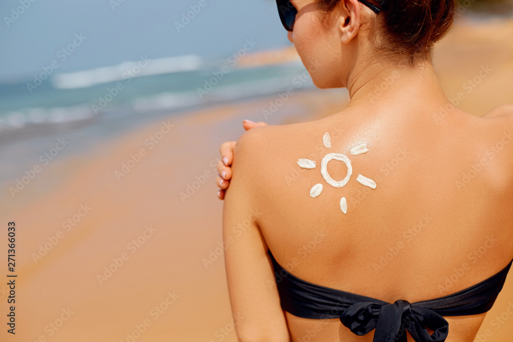 Fototapeta premium Young woman with sun shape on the shoulder holding sun cream bottle on the beach